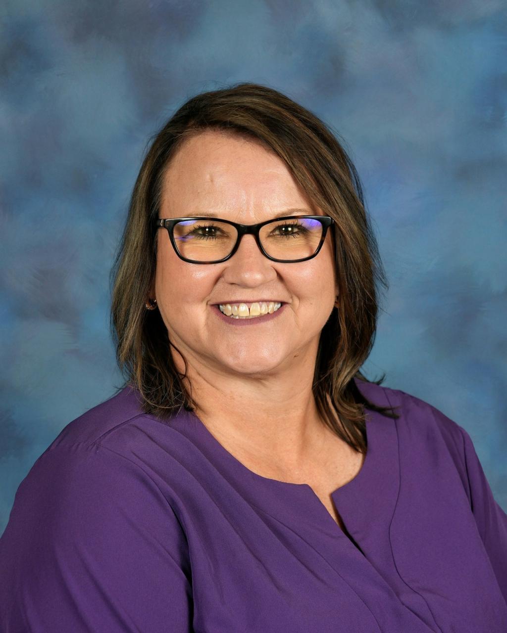 Lady with brown hair, wearing glasses and a purple shirt